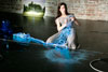 performer in a grey dress kneeling amongst artworks and pulling a rope of blue light across her body
